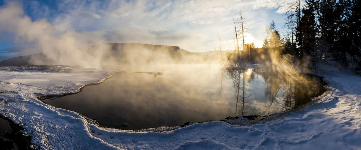 A geothermal hot spring surrounded by snow and trees.