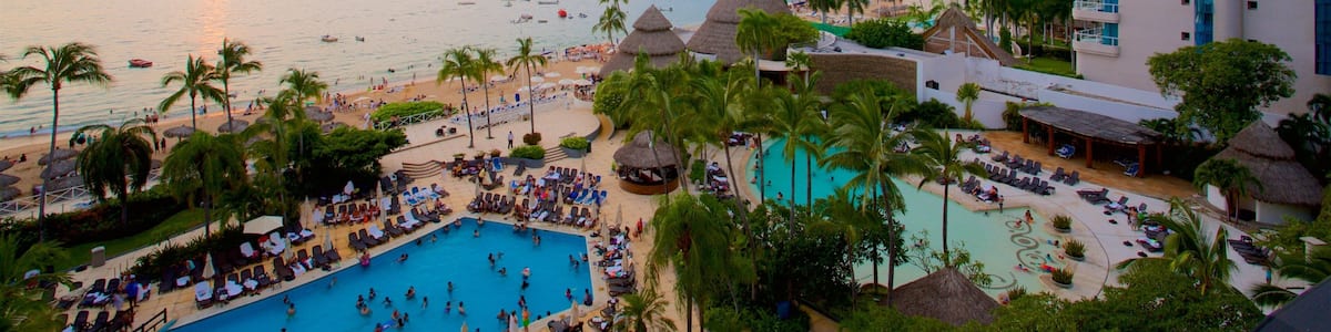 Un complexe hôtelier doté d’une piscine, d’une plage, de palmiers et offrant une vue sur le paysage urbain en arrière-plan.