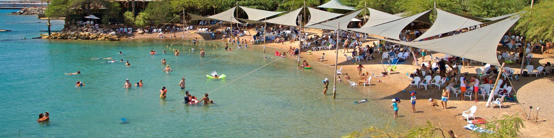 Uma praia movimentada com águas azul-turquesa cristalinas, palmeiras e tendas.