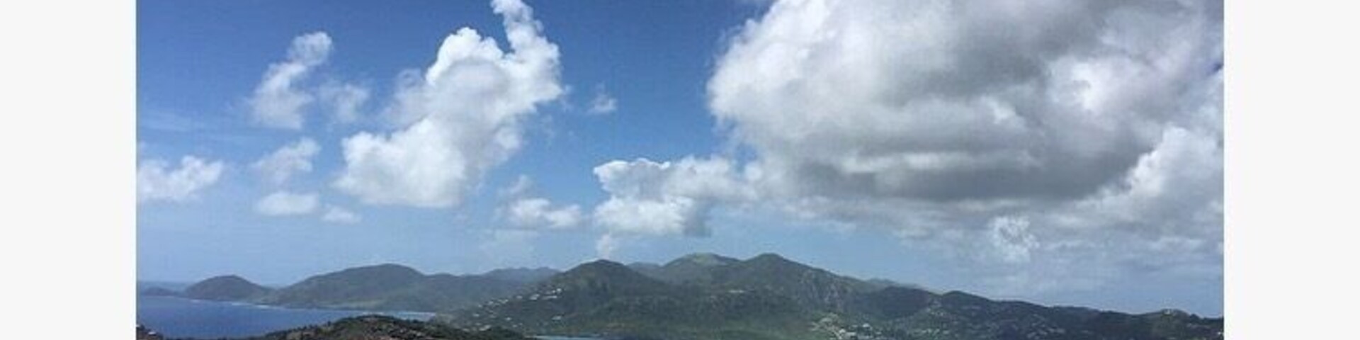 Paisagem costeira com céu claro, uma baía e montanhas ao longe.