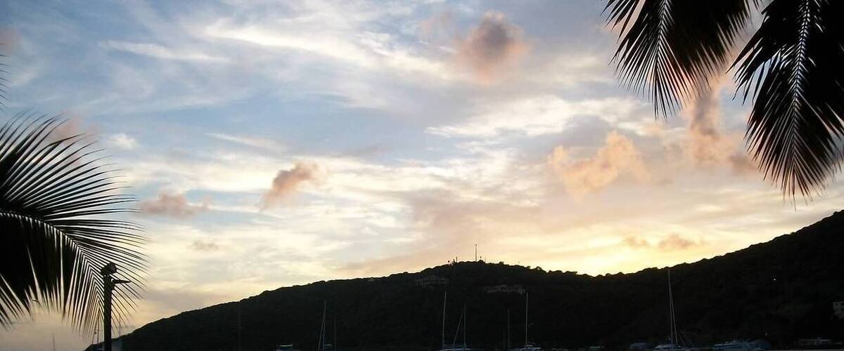 A sunset over a calm harbor with boats, a dock, and chairs along the shore.