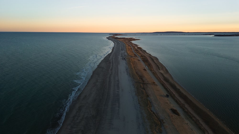 An aerial view of a long, narrow beach with a gentle curve, bordered by calm sea waters.