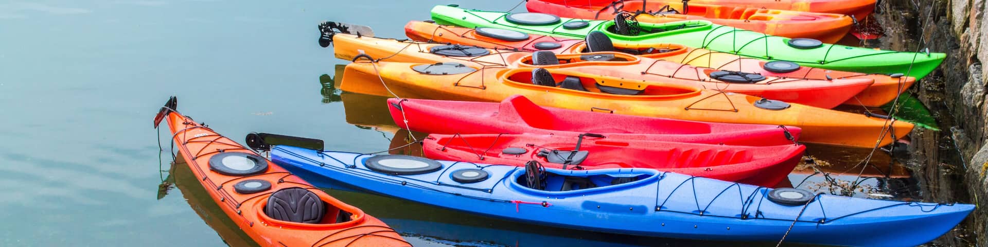 a row of colorful fiberglass kayaks for rent in a small Massachusetts harbor