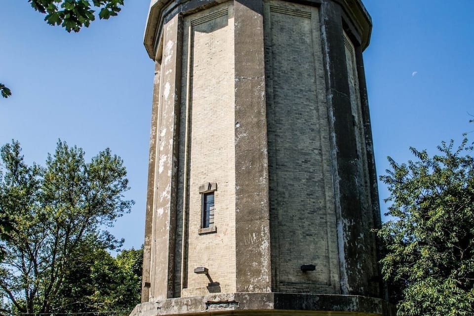 A tall, cylindrical tower with a conical roof, surrounded by trees and a grassy area.
