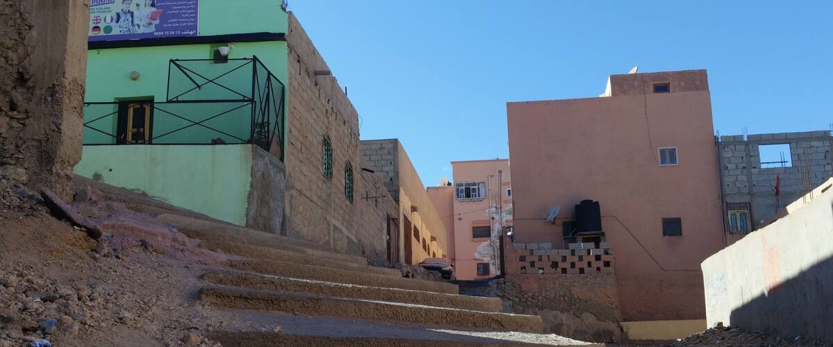 A street with steps leading up to a building with a green facade and a signboard.