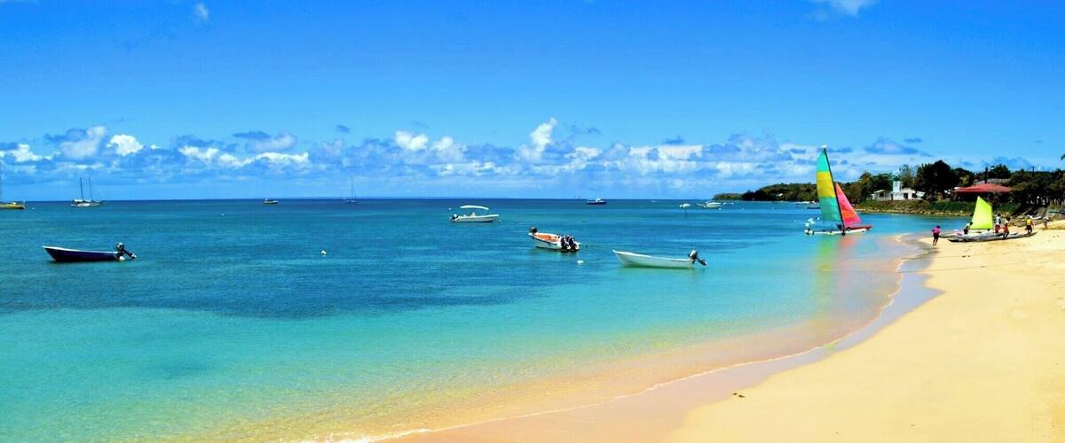A beach with clear turquoise water, a sandy shore, and several sailboats.