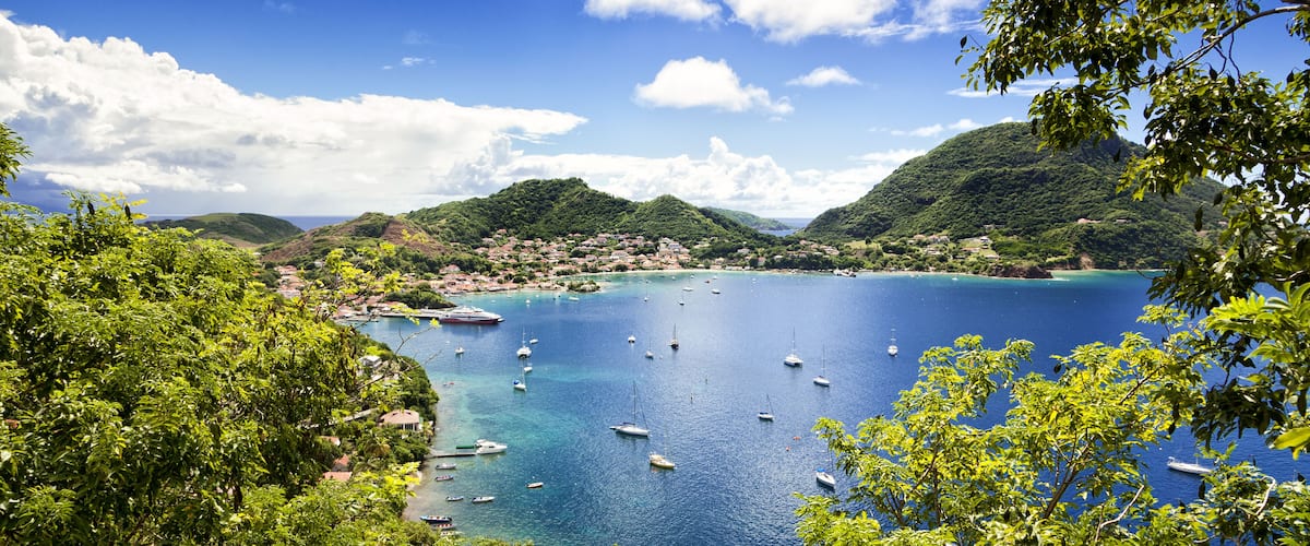 A coastal town with a bay filled with boats, surrounded by lush green hills and clear blue waters.
