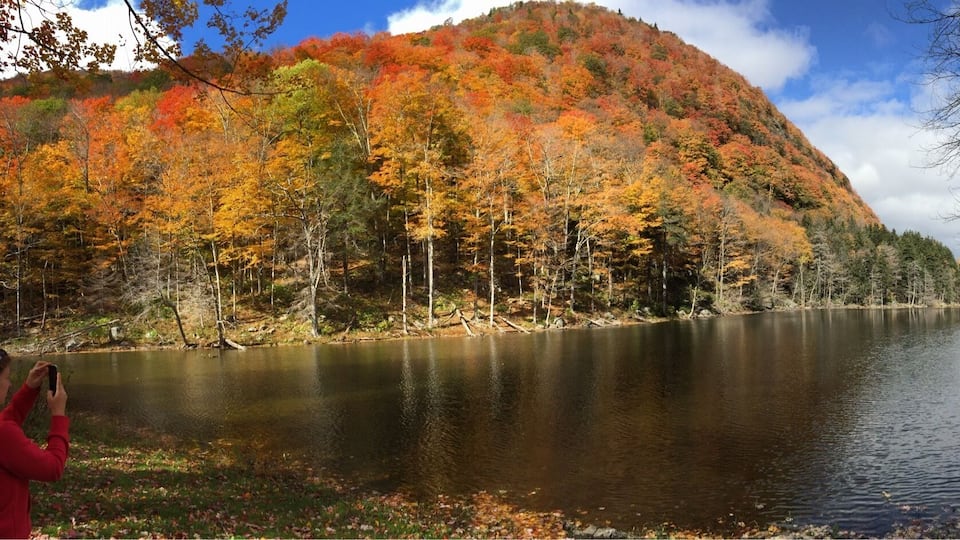 A calm river with autumn foliage and hills in the background.