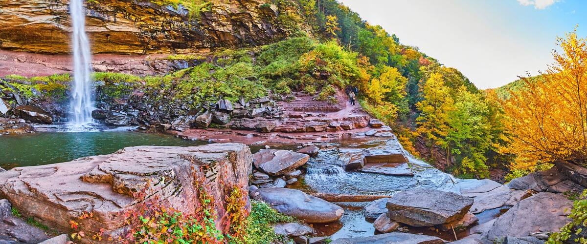 A waterfall cascading into a river surrounded by autumn-colored trees and rocky terrain.