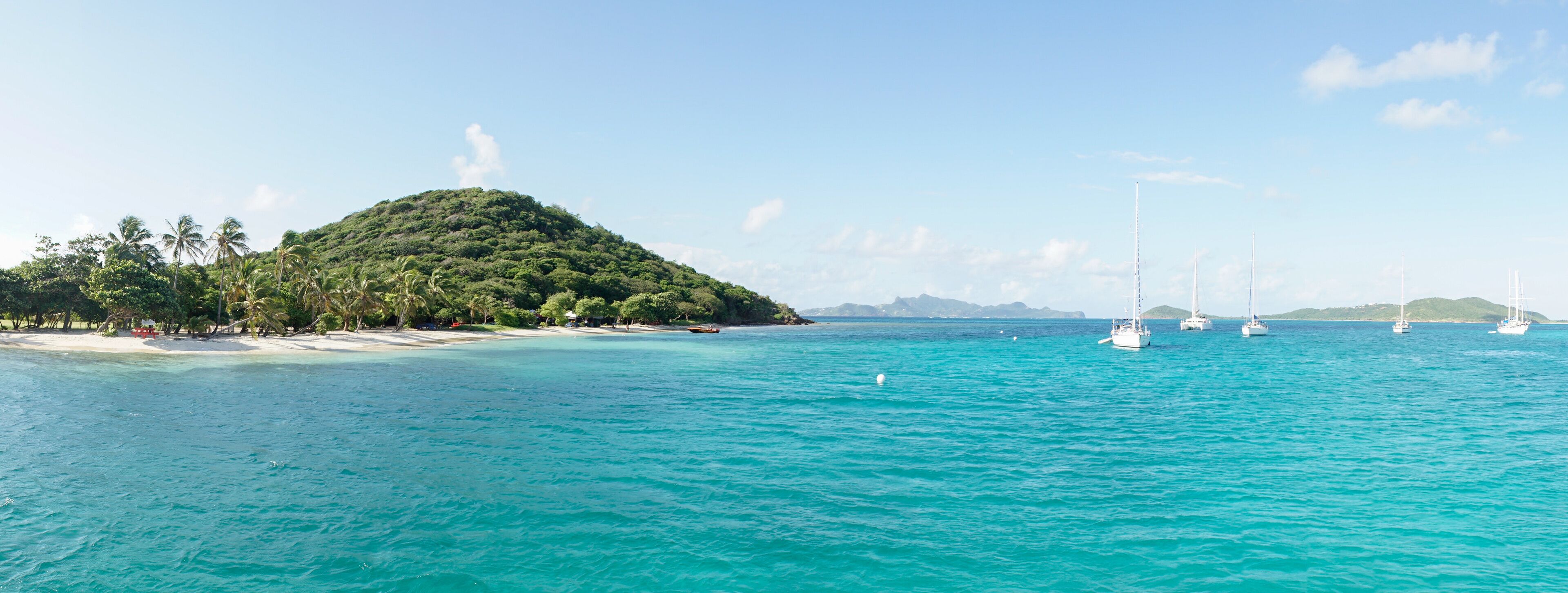 A tropical island with clear turquoise waters, a sandy beach, and several sailboats.