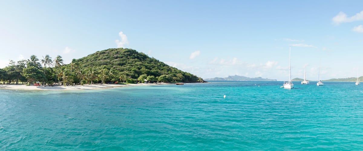 A tropical island with clear turquoise waters, a sandy beach, and several sailboats.