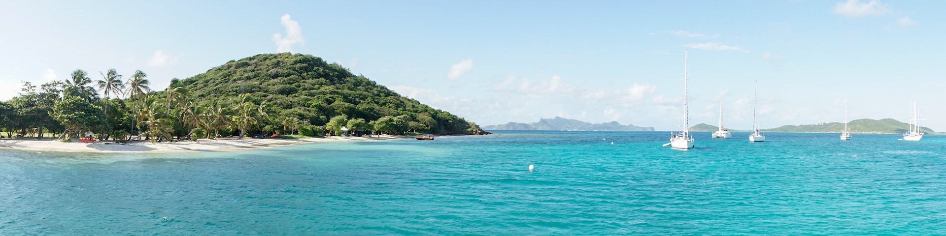 A tropical island with clear turquoise waters, a sandy beach, and several sailboats.