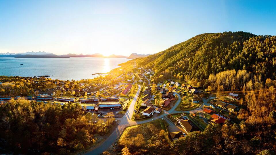 An aerial view of a coastal town with a mountain, dense forest, and a body of water.