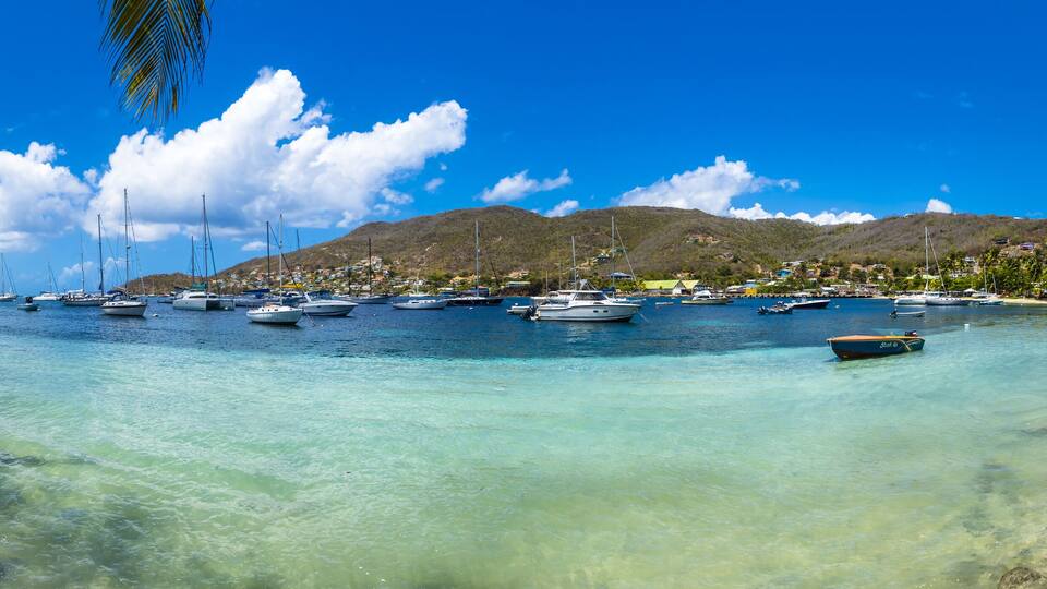 A marina with numerous boats docked, clear turquoise water, and a mountainous backdrop.