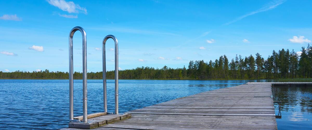 A wooden dock extending into a calm lake with metal railings on one end.