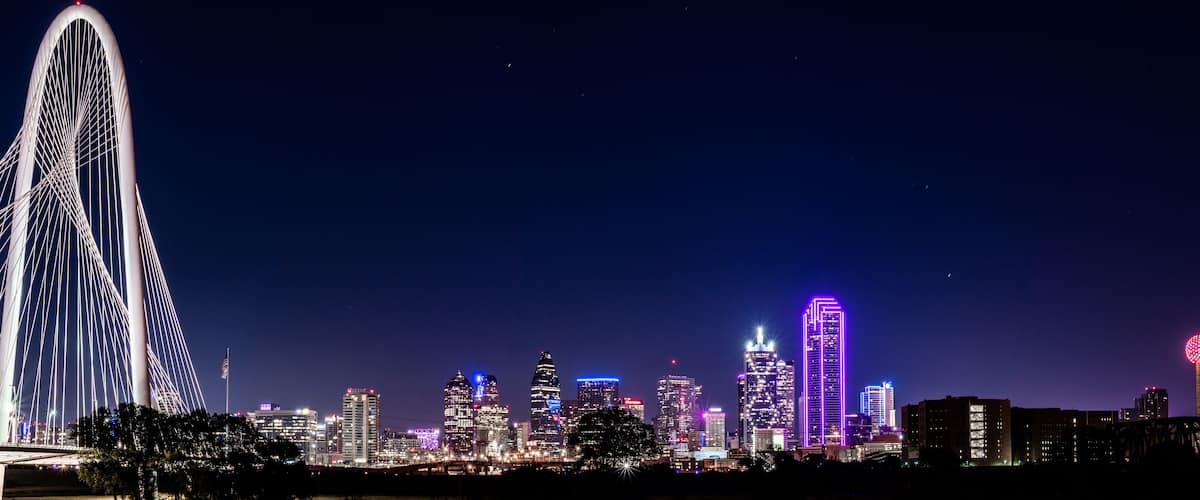 A city skyline at night with illuminated buildings and a prominent bridge.