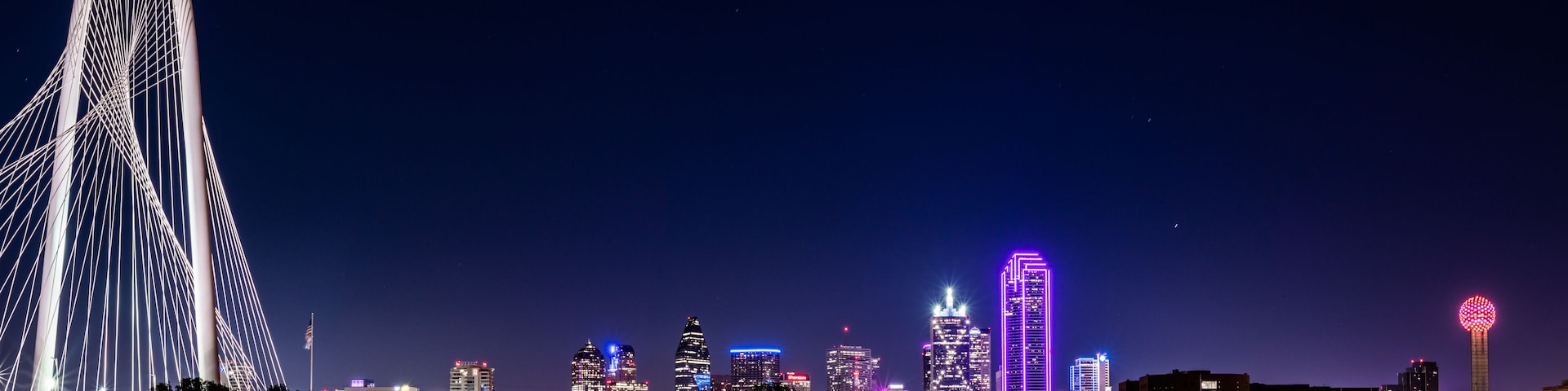 A city skyline at night with illuminated buildings and a prominent bridge.