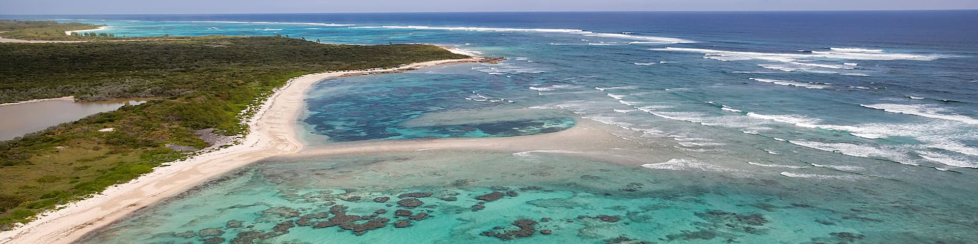 A coastal landscape with clear turquoise waters, a sandy beach, and visible coral formations.