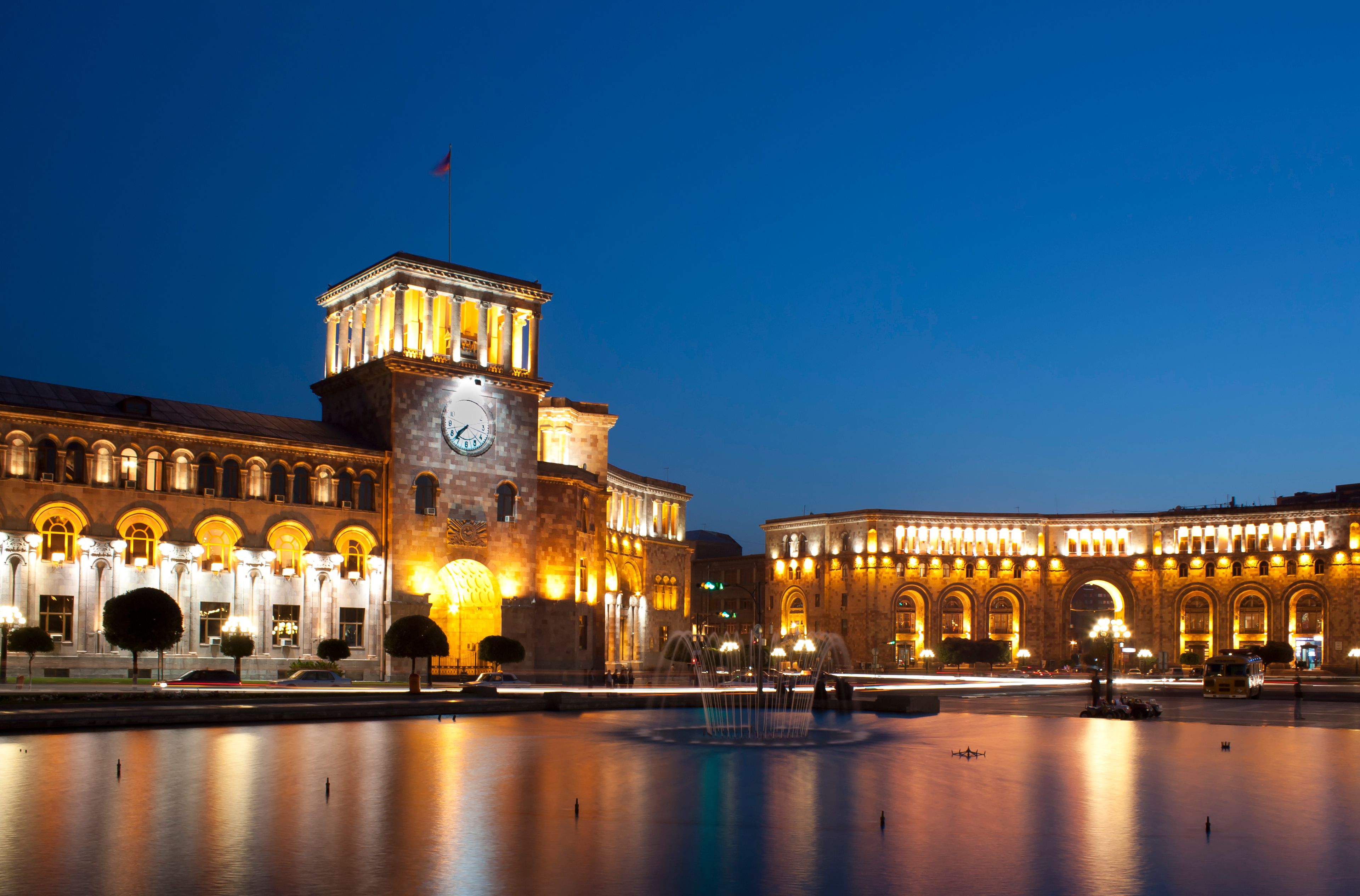 A historic building with a clock tower and classical architecture, reflecting in a calm water body.
