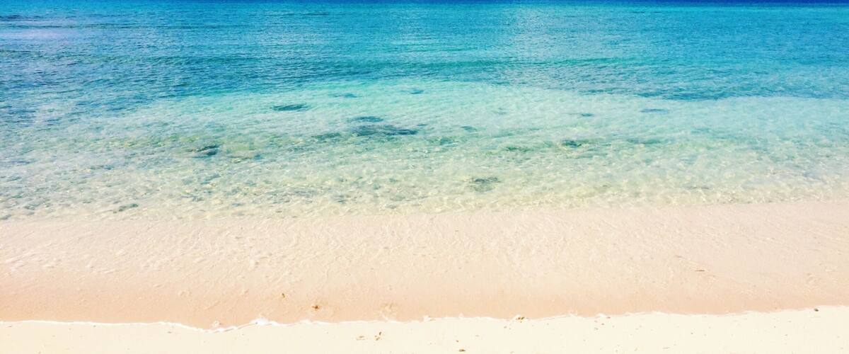 A clear turquoise sea, white sandy beach, and a bright blue sky with fluffy clouds.