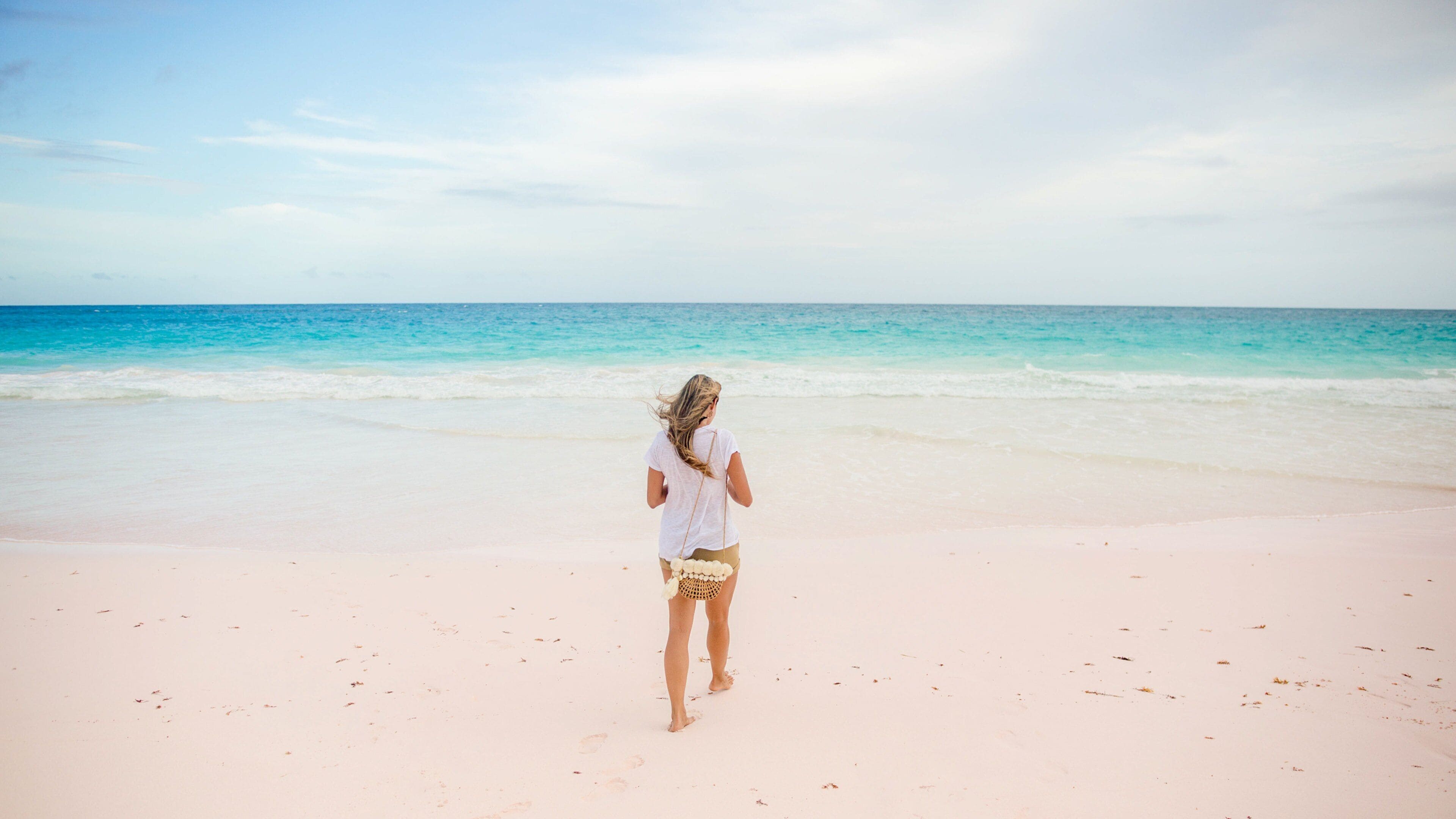 A woman walking on a sandy beach with a clear sky and calm sea.