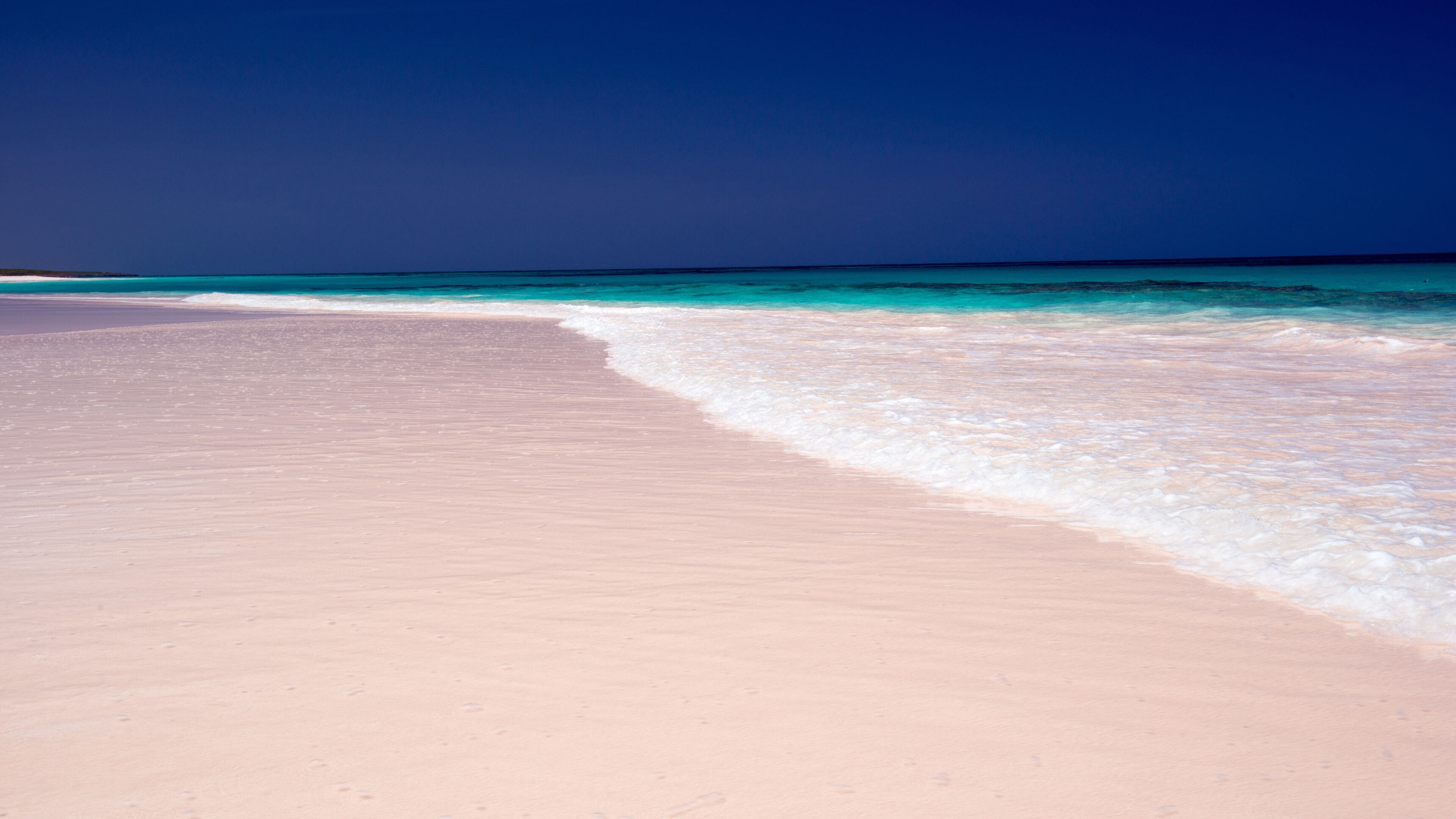A pink sandy beach with turquoise waters.