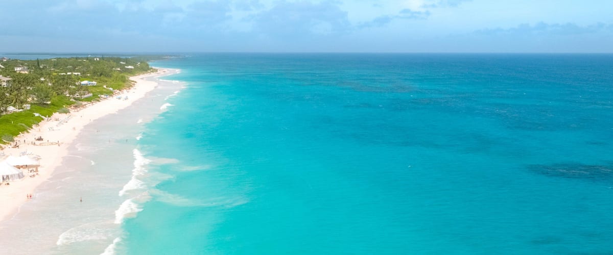 A turquoise coastline with a sandy beach and a forested area.