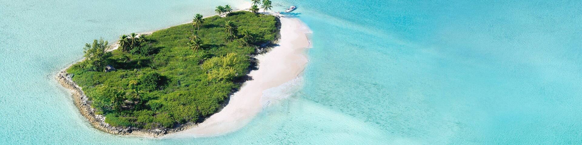 An aerial view of a small island with a sandy beach, surrounded by clear turquoise waters.
