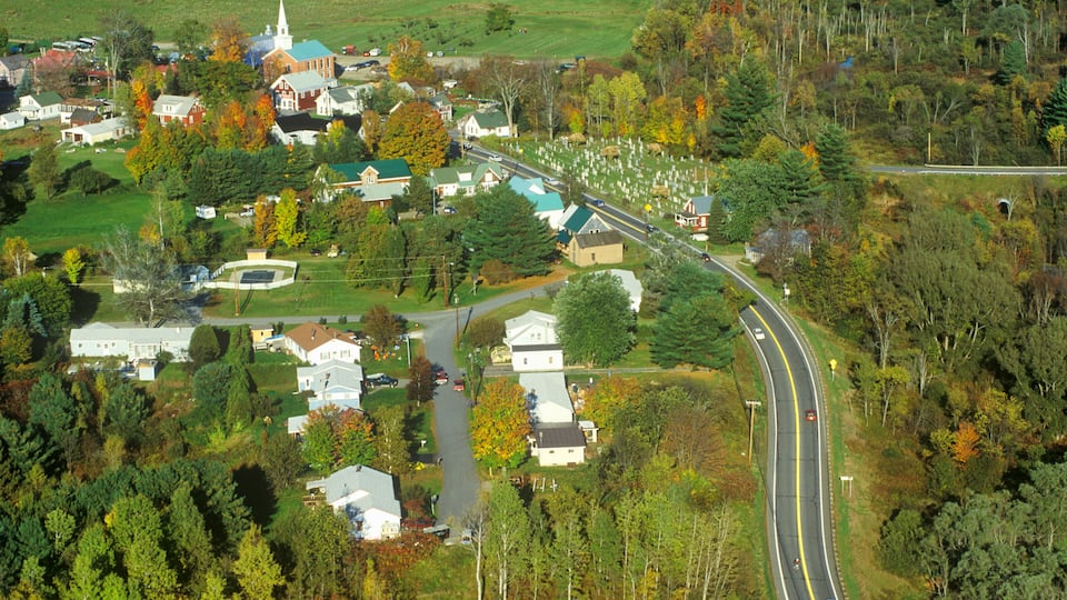 A rural town with a church, houses, and a winding road through a forested area.