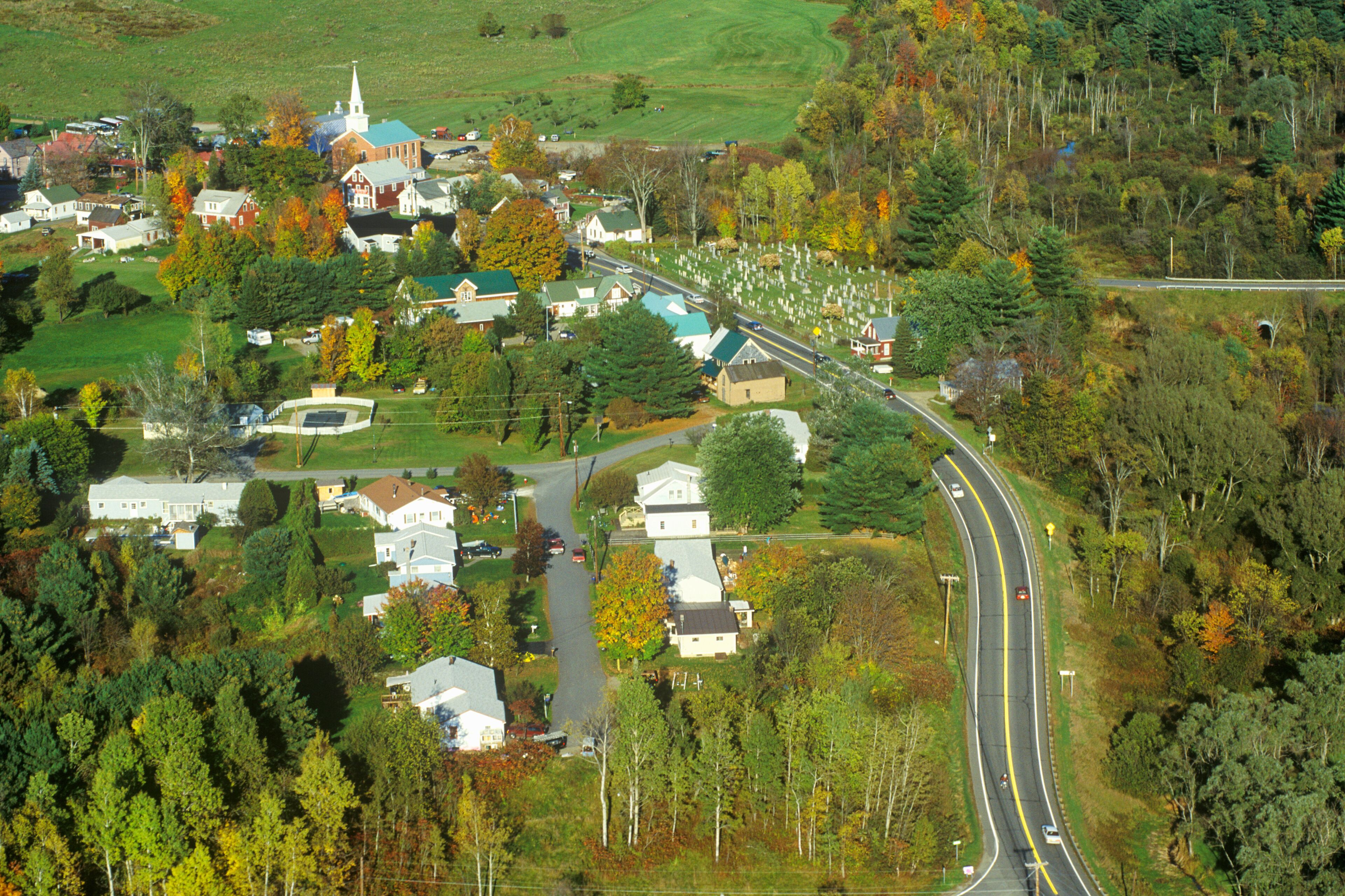 A rural town with a church, houses, and a winding road through a forested area.