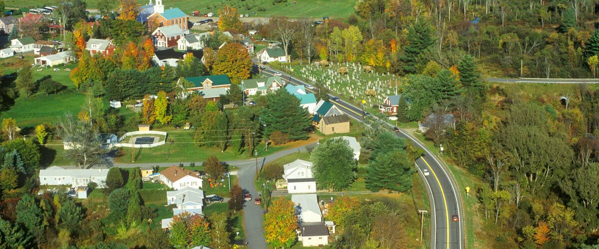 A rural town with a church, houses, and a winding road through a forested area.