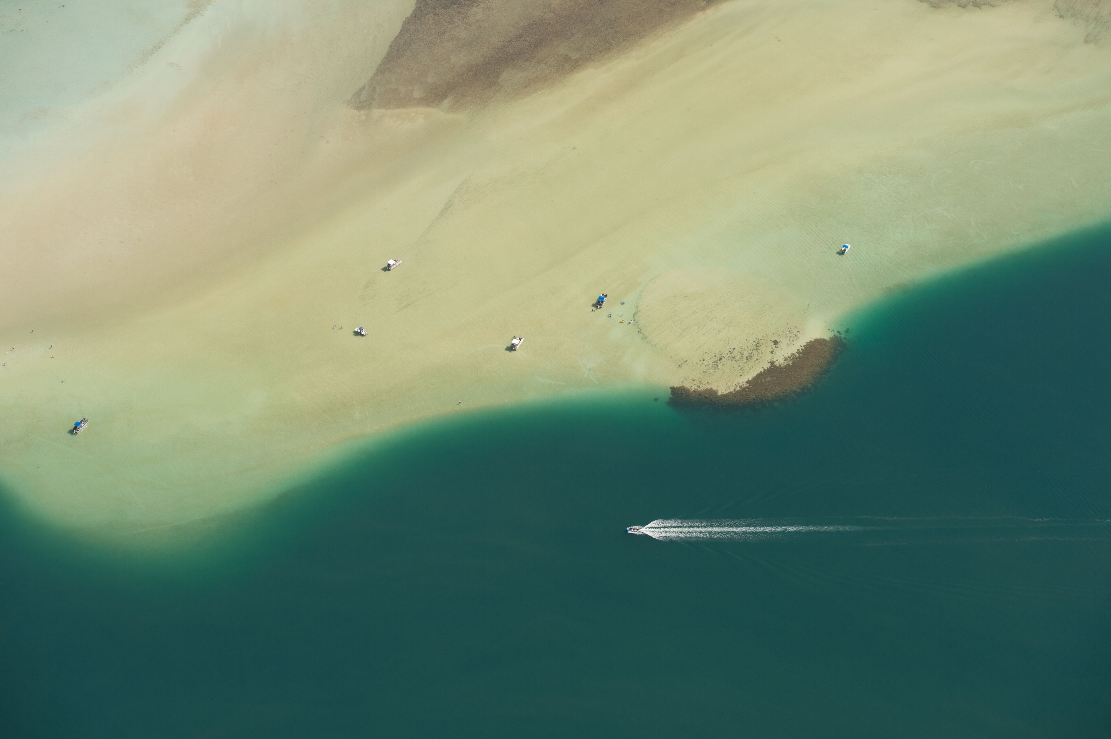 Vista aérea de una playa con aguas turquesas cristalinas, una orilla arenosa y algunas personas dispersas a lo largo de la playa.