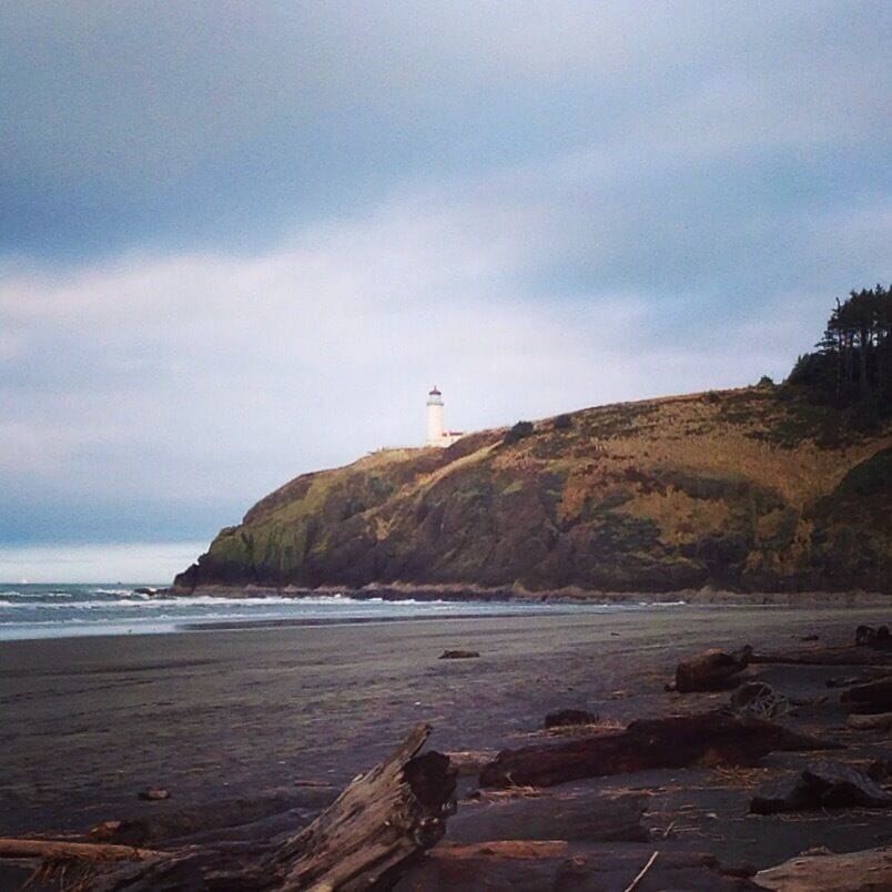 A rocky beach with a lighthouse on a hill.