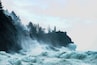 A lighthouse on a rocky cliff with waves crashing against it.