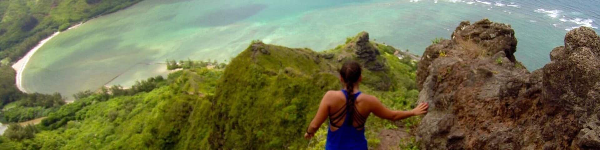 A woman hiking on a trail overlooking a coastal landscape with lush greenery and turquoise waters.