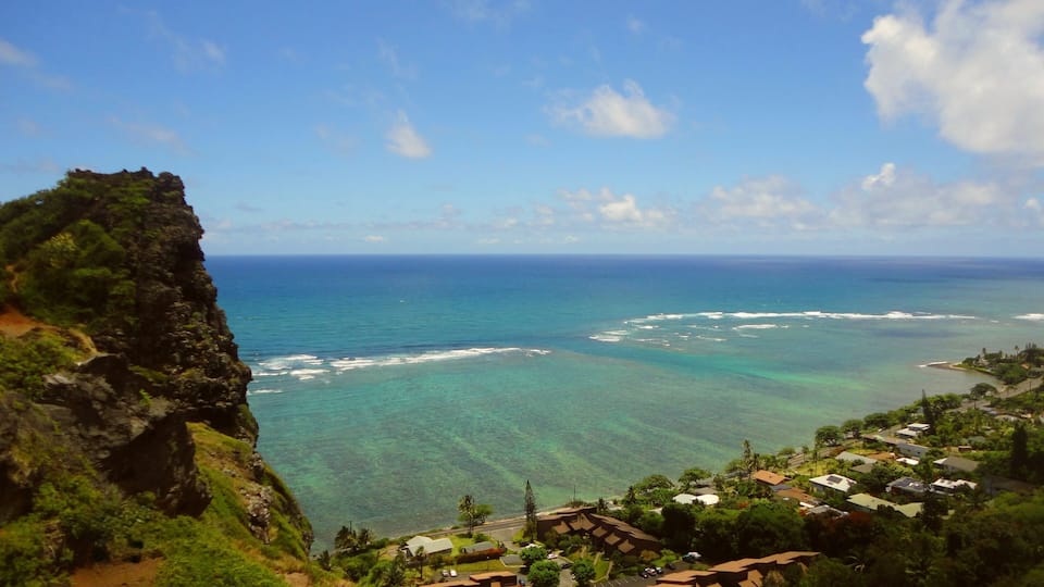 A coastal landscape with a clear view of the ocean, a rocky cliff, and a residential area with houses.