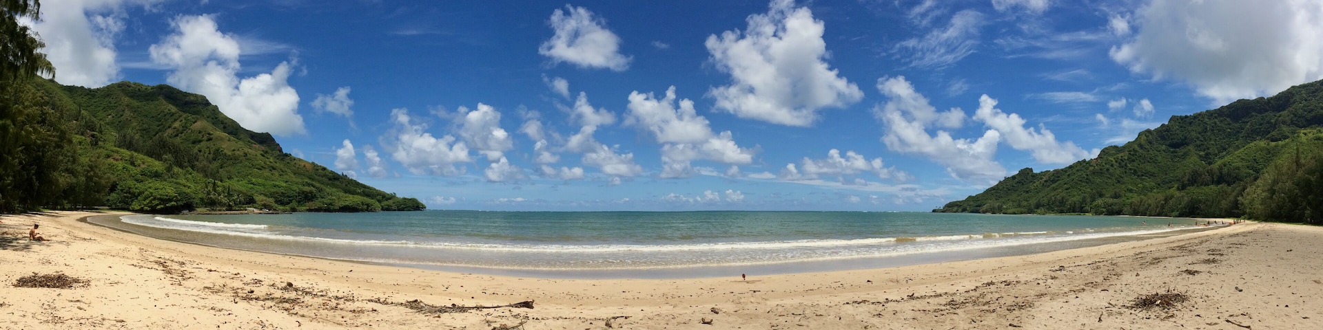 A beach with clear blue water, sandy shore, and green hills in the background.