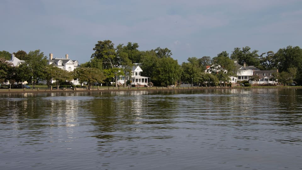 A calm lake with white houses and trees along the shore.
