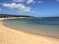 A sandy beach with clear water, a boat, and a distant shoreline with buildings and trees.