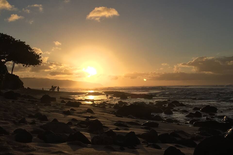 A beach with rocks and the sun setting over the ocean.