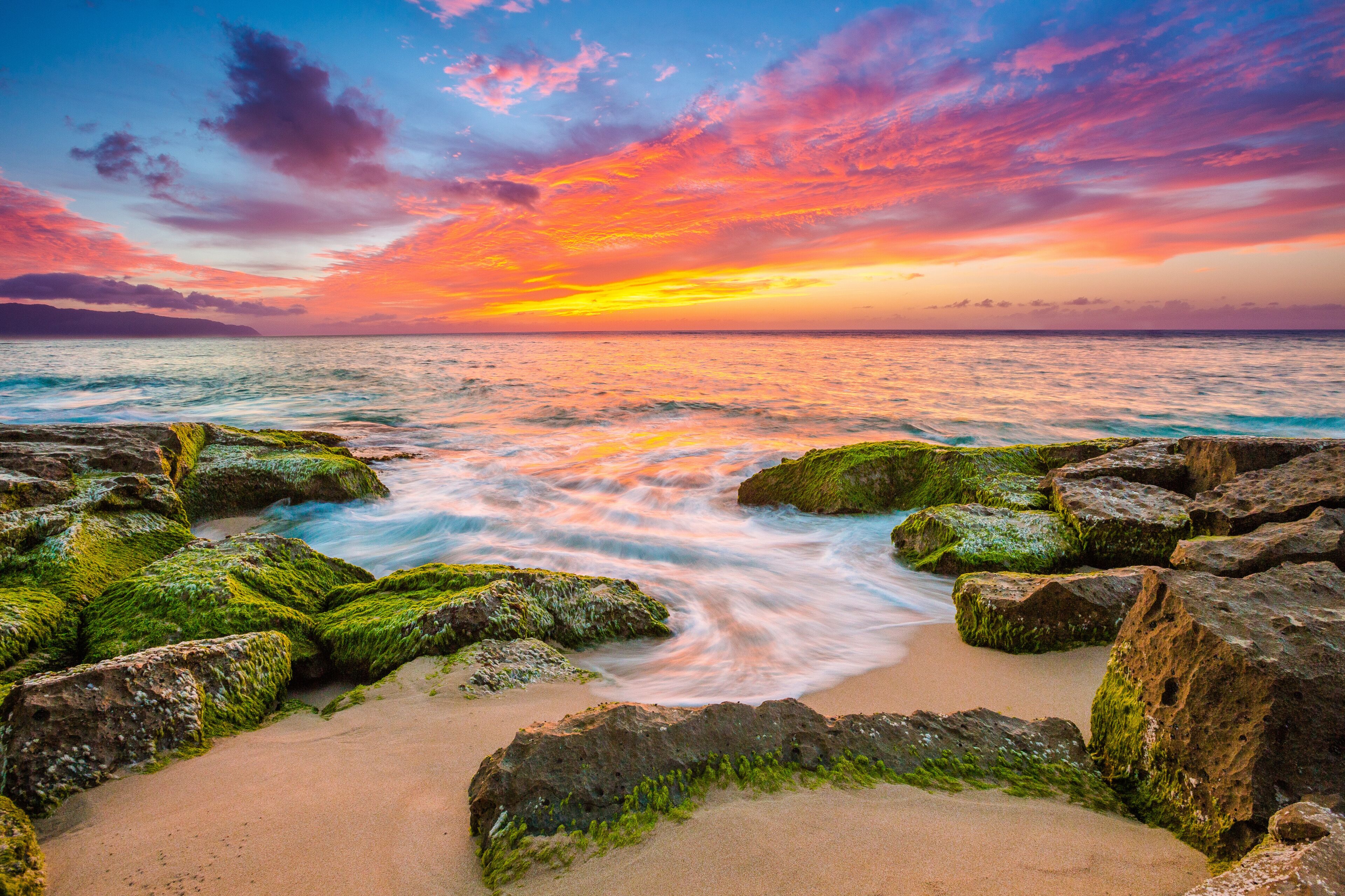 A sunset over a rocky beach with waves.