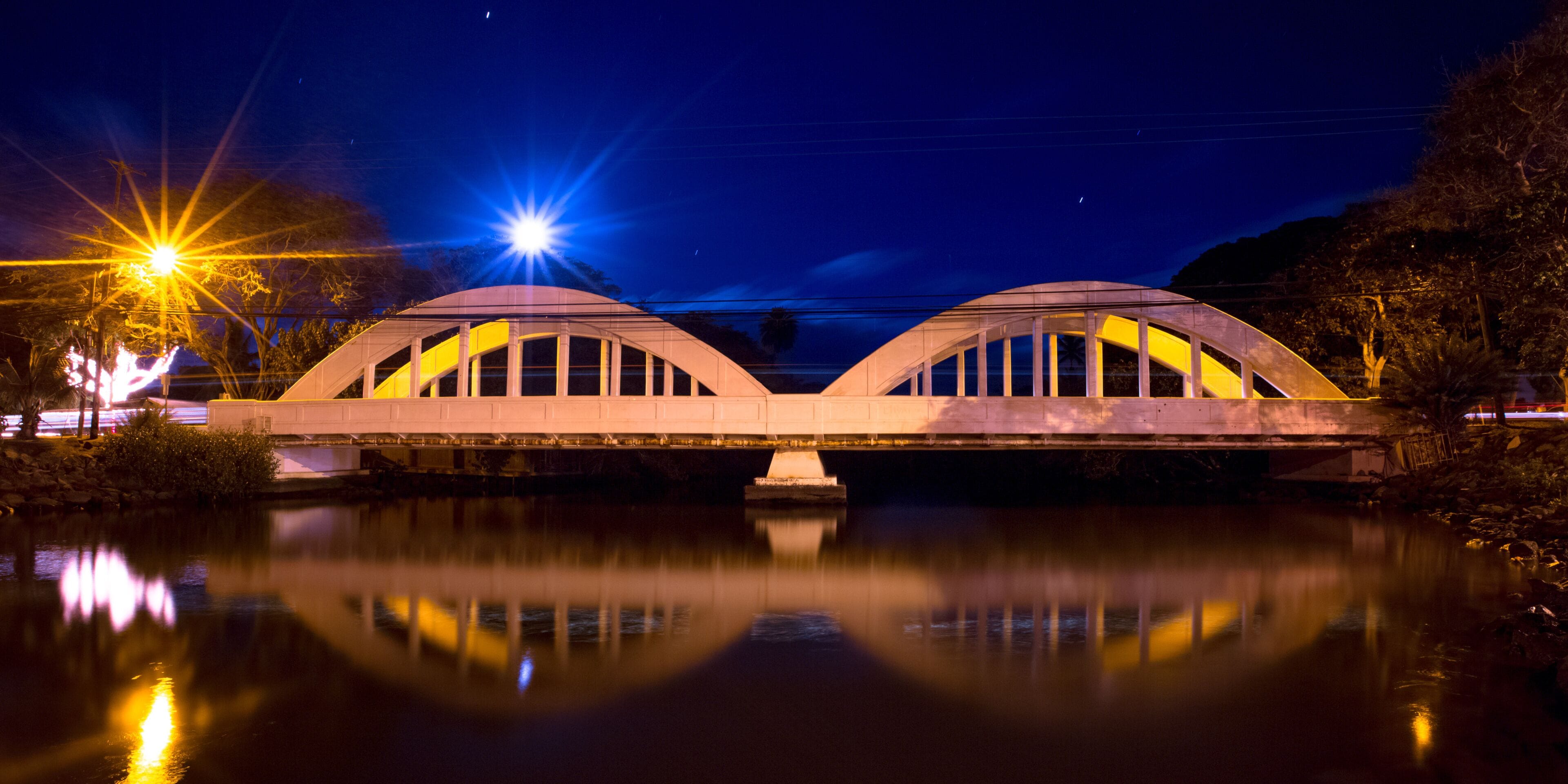 A bridge with two arches over a calm river, illuminated by streetlights.