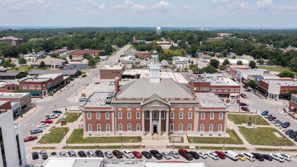 A large brick building with a central dome and clock tower, surrounded by a parking lot and streets.
