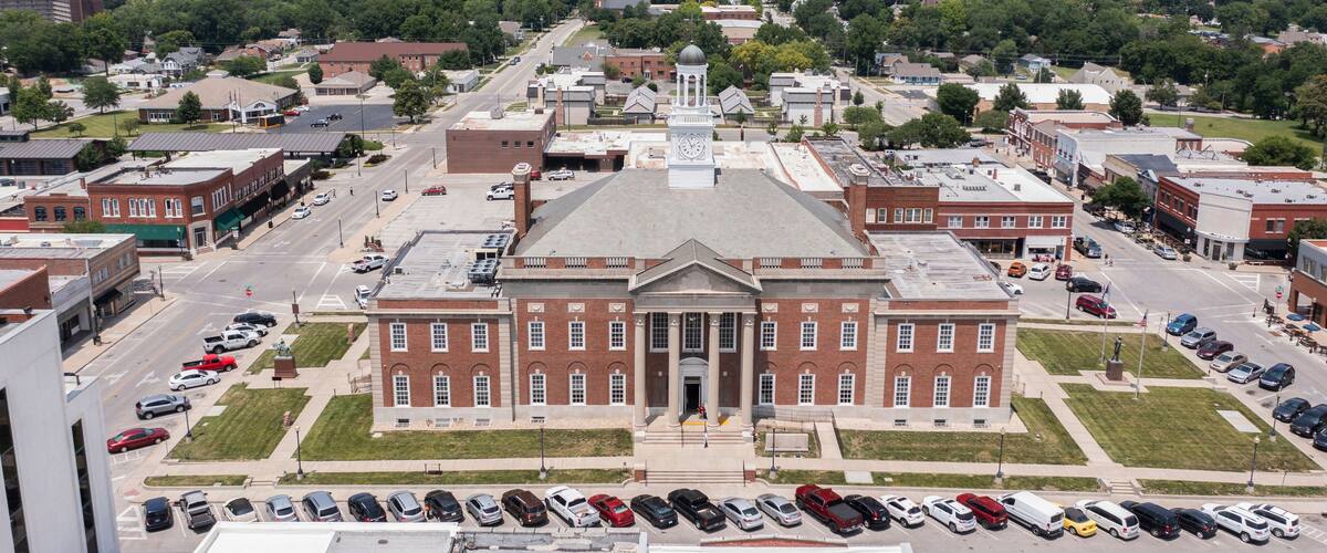 A large brick building with a central dome and clock tower, surrounded by a parking lot and streets.