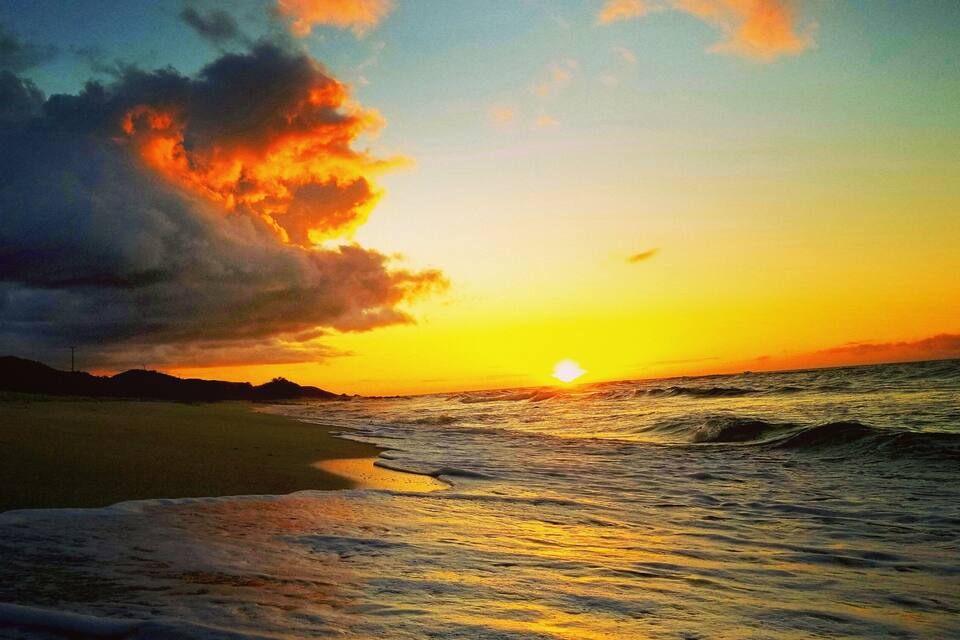 Pôr do sol sobre uma praia com ondas e céu nublado.