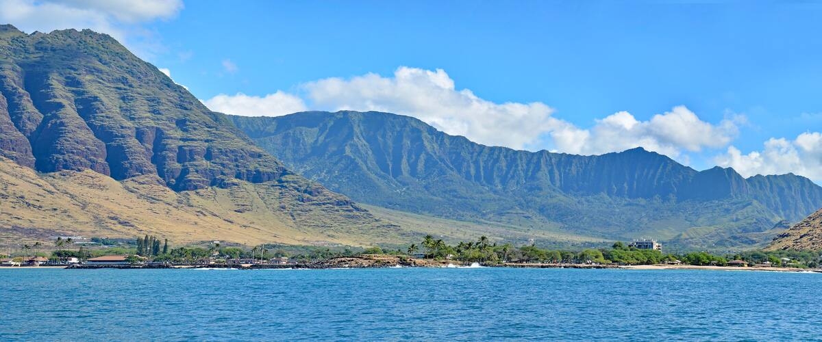 A coastal landscape with mountains, a beach, and a clear blue sky.
