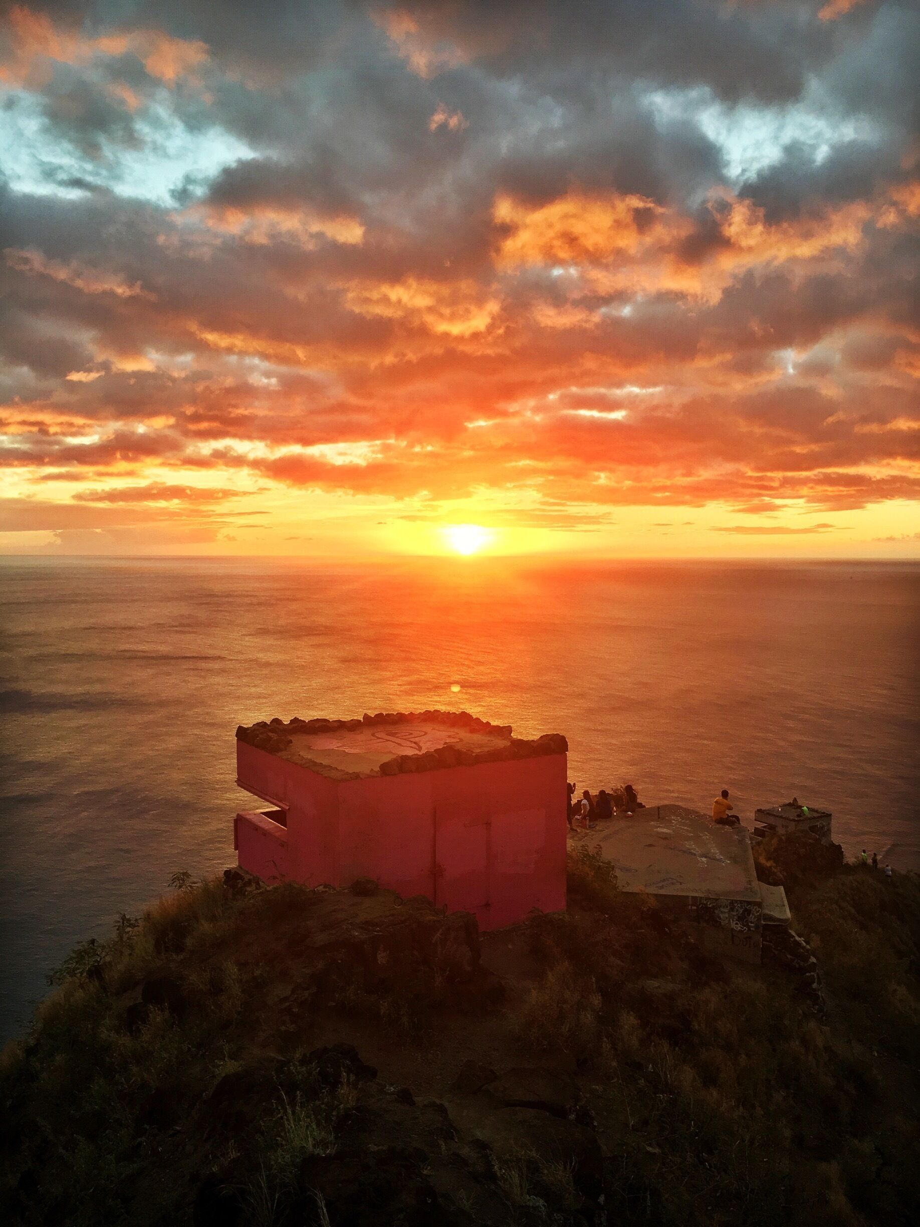 A sunset over the ocean with a rocky outcrop in the foreground.