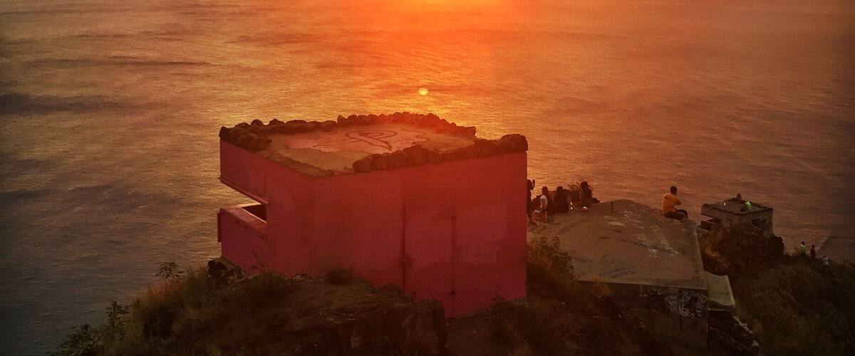A sunset over the ocean with a rocky outcrop in the foreground.
