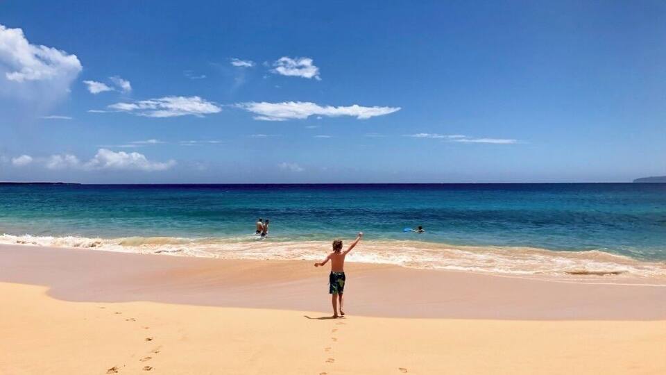 A beach with footprints leading to the water, a clear sky, and a few people in the distance.