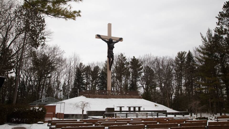 A wooden bench area, a large cross, and a building with a snow-covered roof.